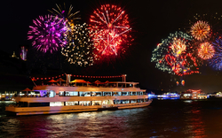 Schiff auf einem Fluss am Abend mit Feuerwerk am Himmel.