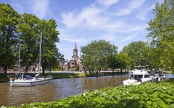 Boote fahren auf einem Fluss an einer Kirche und Bäumen vorbei.