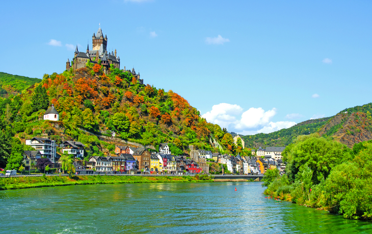 Burg auf einem Hügel über einer Stadt am Flussufer bei klarem Himmel.