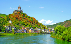 Burg auf einem Hügel über einer Stadt am Flussufer bei klarem Himmel.