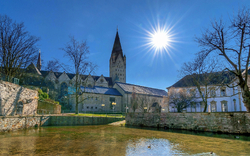 Kirche an einem sonnigen Tag mit klarem Himmel und Enten im Wasser.