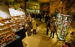 Besucher auf einem Weihnachtsmarkt in einer Höhle mit bunten Ständen und Dekorationen.
